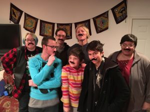 A group of people wearing mustaches pose for a picture