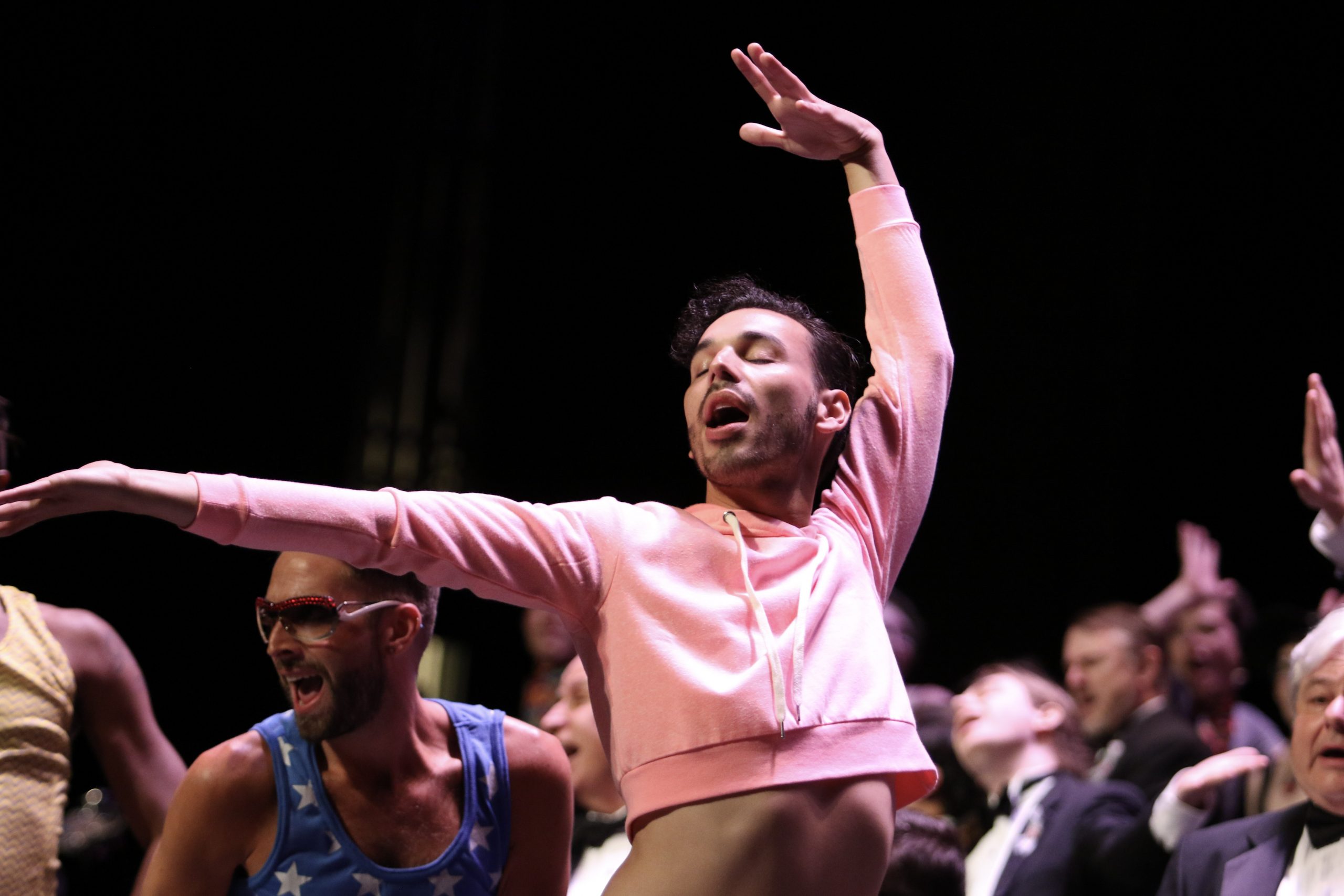 male dancer in pink crop top with singers in the background