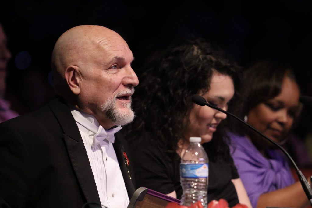 white, bald, male seated at a microphone on a panel with two women