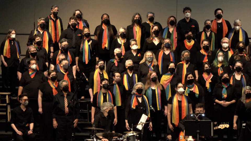 The Portland Lesbian Choir sings, wearing black with rainbow scarves.