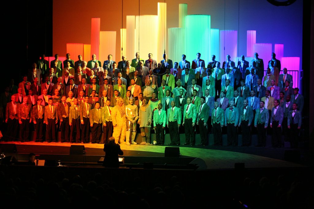 A choir of men with an overlay of a city skyline in rainbow lights