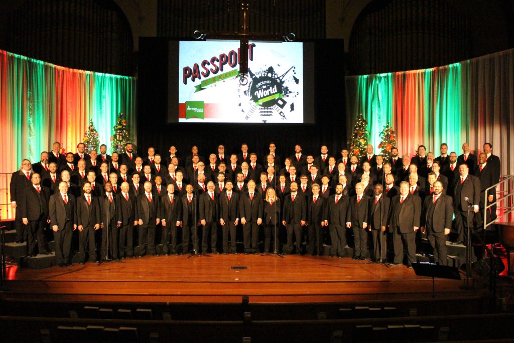Choir of male presenting singers where black tuxedos and red ties standing on risers