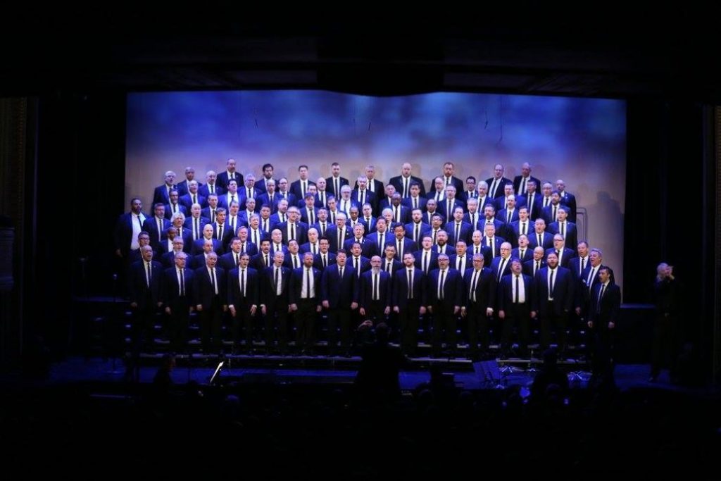 male presenting singers on risers singing wearing suits