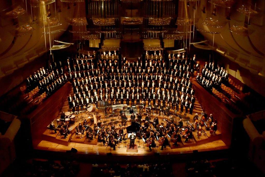 San Francisco Gay Men's Chorus sings in a huge concert hall in front of an orchestra and behind a giant organ