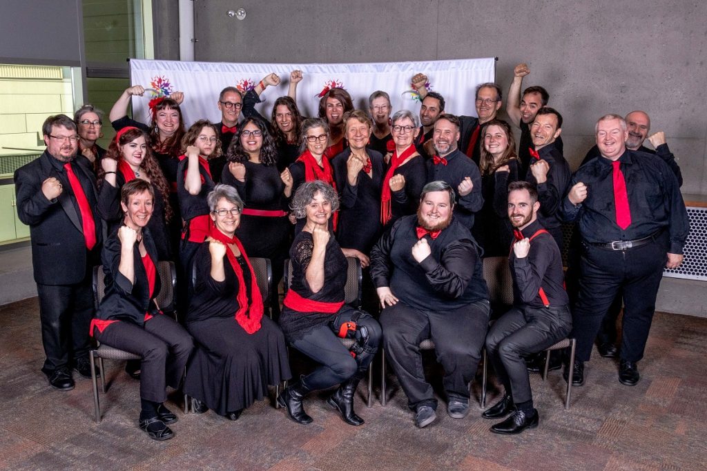 the choir Tone Cluster poses wearing black with red accents, all holding up their right hand in a fist