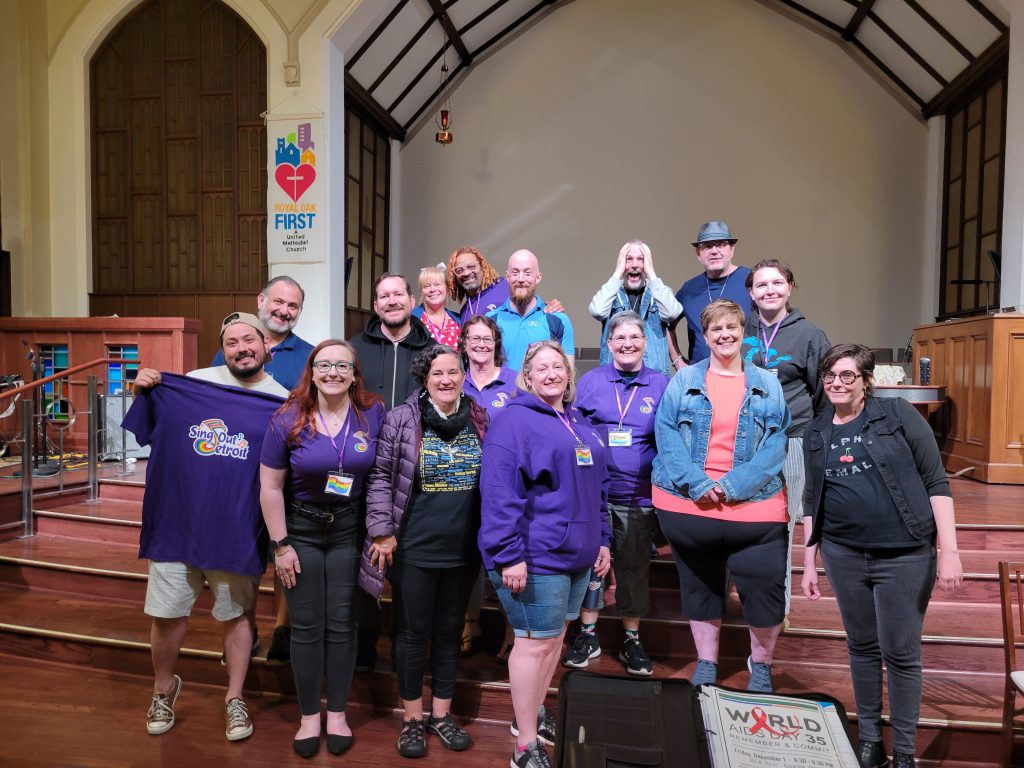 A group of singers, many wearing purple shirts, pose in a church