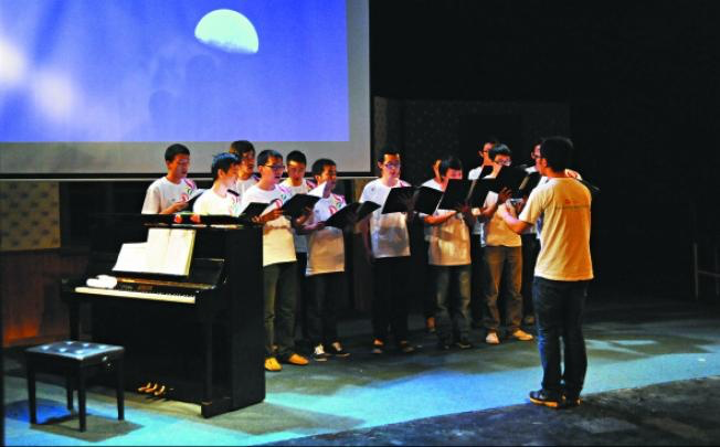A chorus made up of young members performs, a conductor in the foreground. 