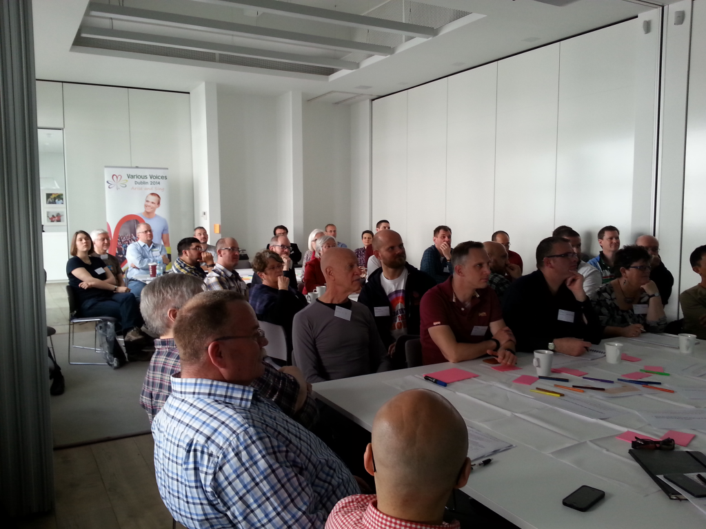 A group of people with name tags sit at tables, giving their attention to a source off-screen.