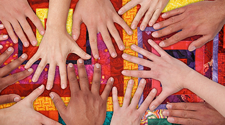 A diverse group of people place their hands together on a colorful background. 