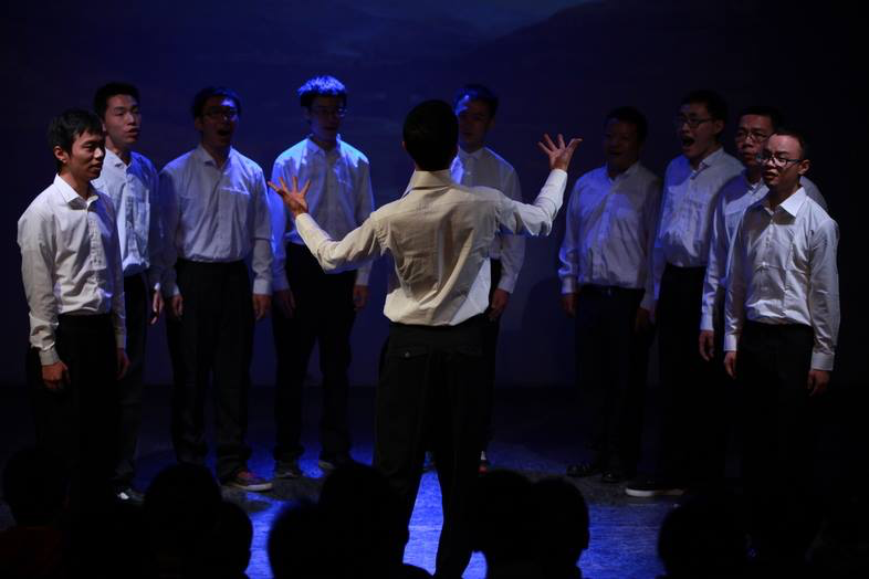 A group of singers gather around a conductor on a stage.