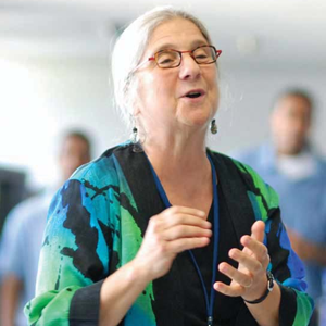 Cathy Roma conducts a chorus wearing a blue and green flowing top.