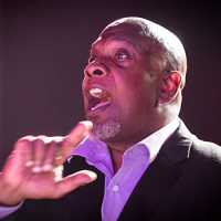 Steve Milloy conducts, wearing a purple shirt under a black blazer.