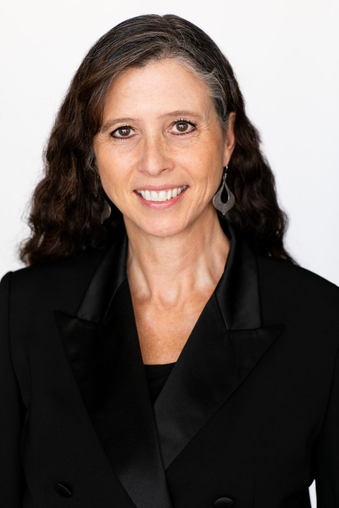 Dr. Elizabeth Scahuer smiles in front of a white background with long dark hair and a dark suit.