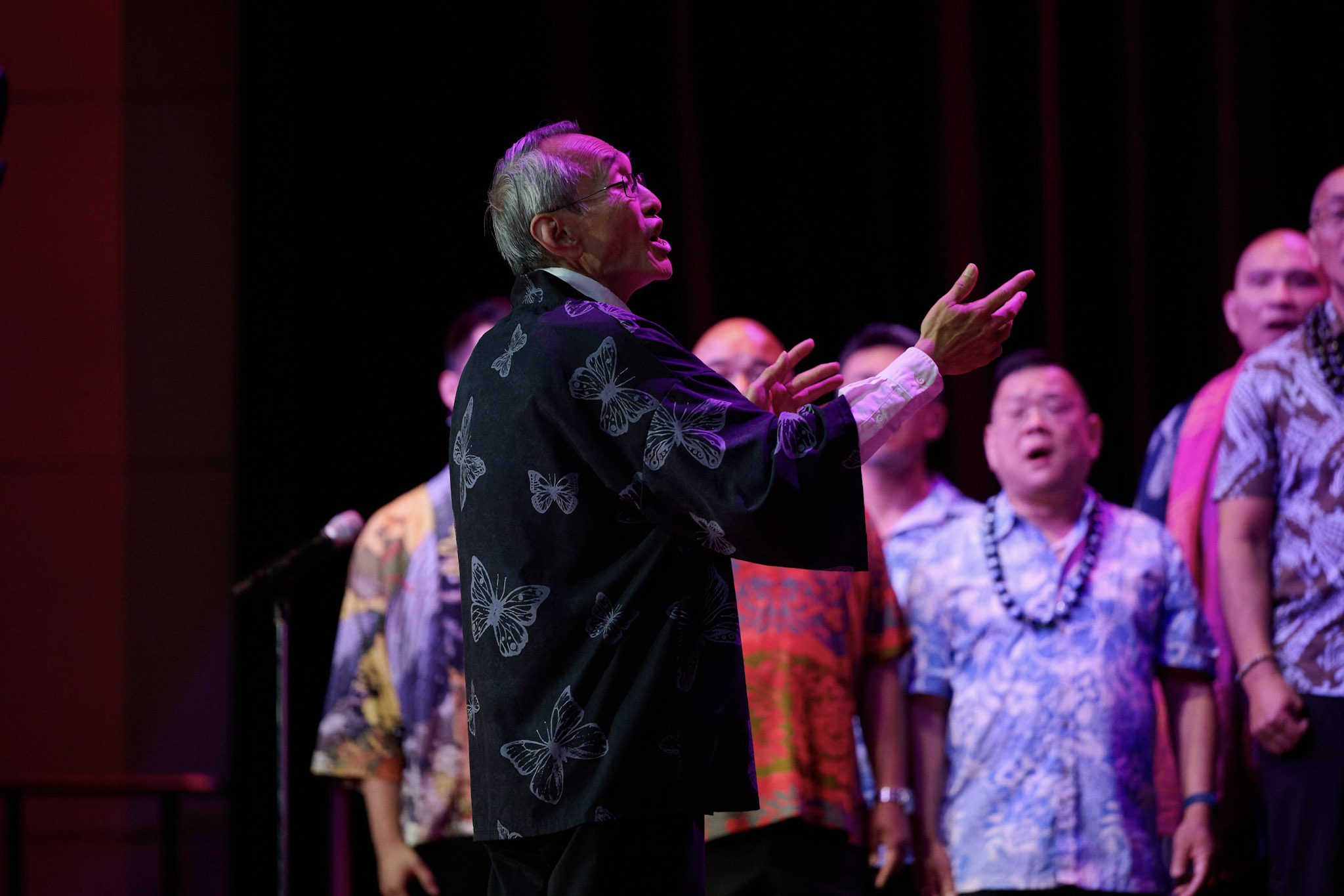 Randy Kikukawa conducts GAPA Men’s Chorus at Festival 2024 in Minneapolis, dressed in printed butterfly shirt.