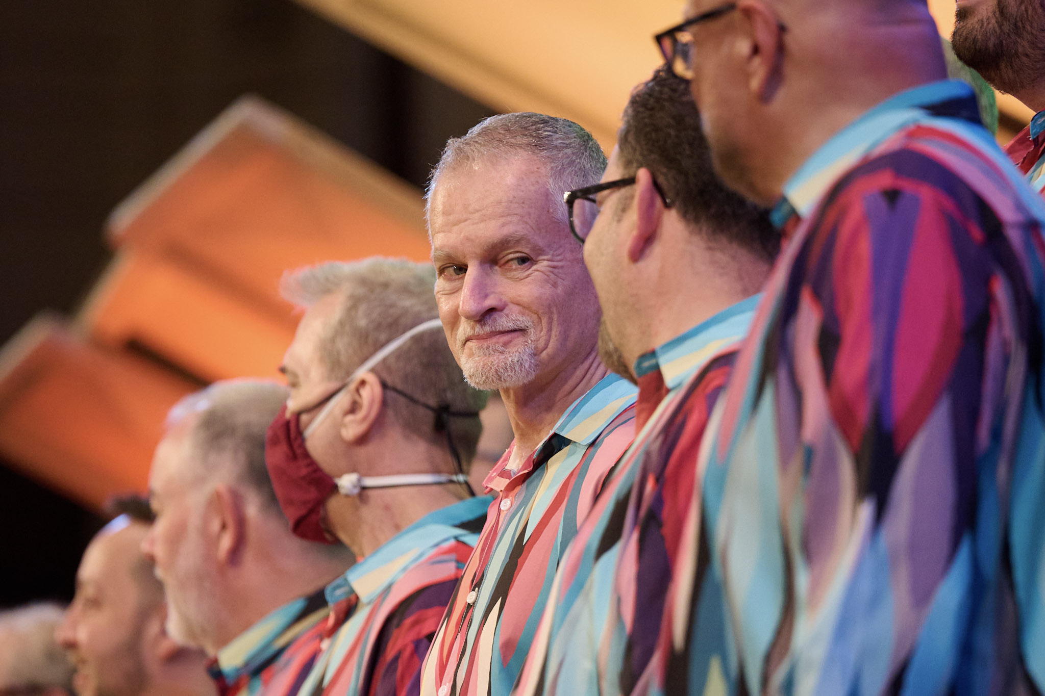 A singer at Festival 2024 looks at a fellow singer, both wearing colorful shirts.