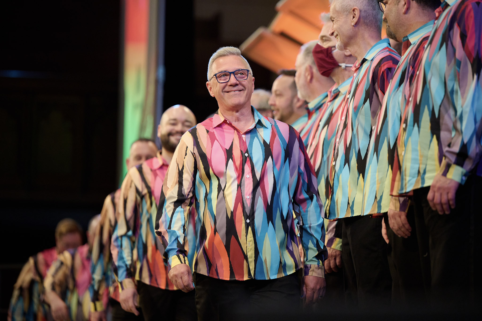 A singer at Festival 2024 smiles, wearing colorful shirts.