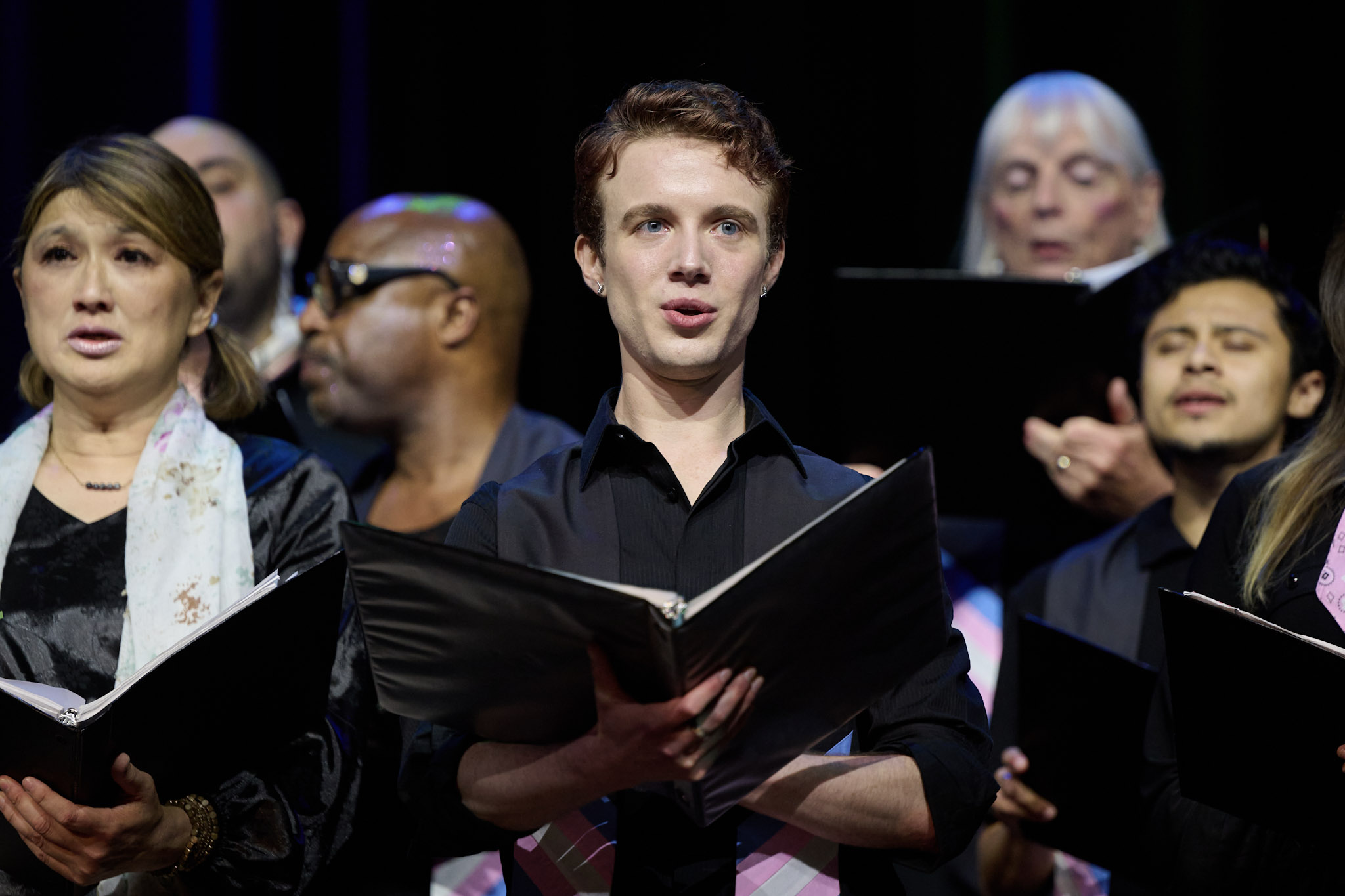 A singer with short brown hair in the Trans Chorus of LA sings on stage at Festival 2024, wearing a black shirt.