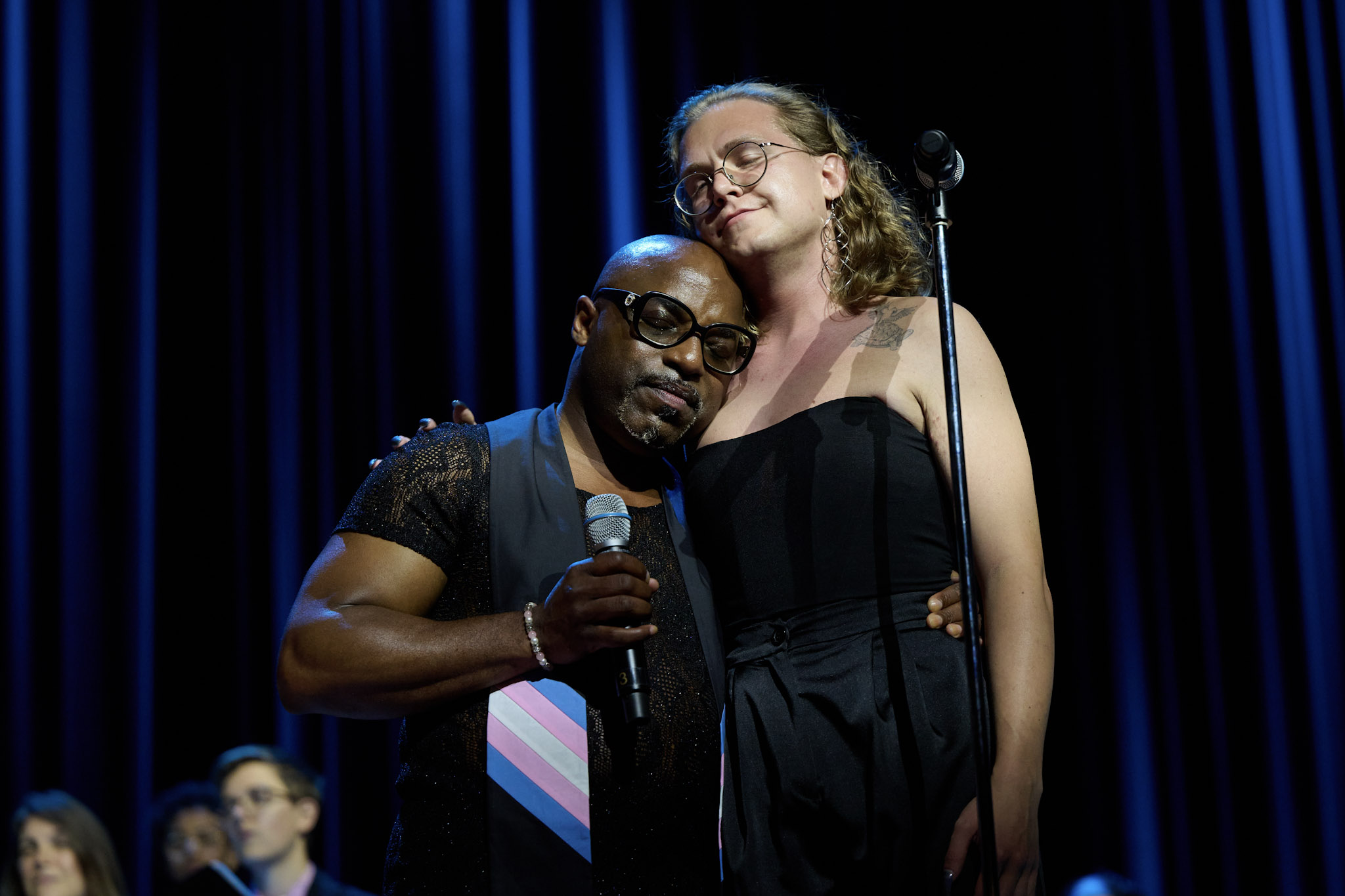 Two singers hug at Festival 2024 in Minneapolis in front of a blue curtain.