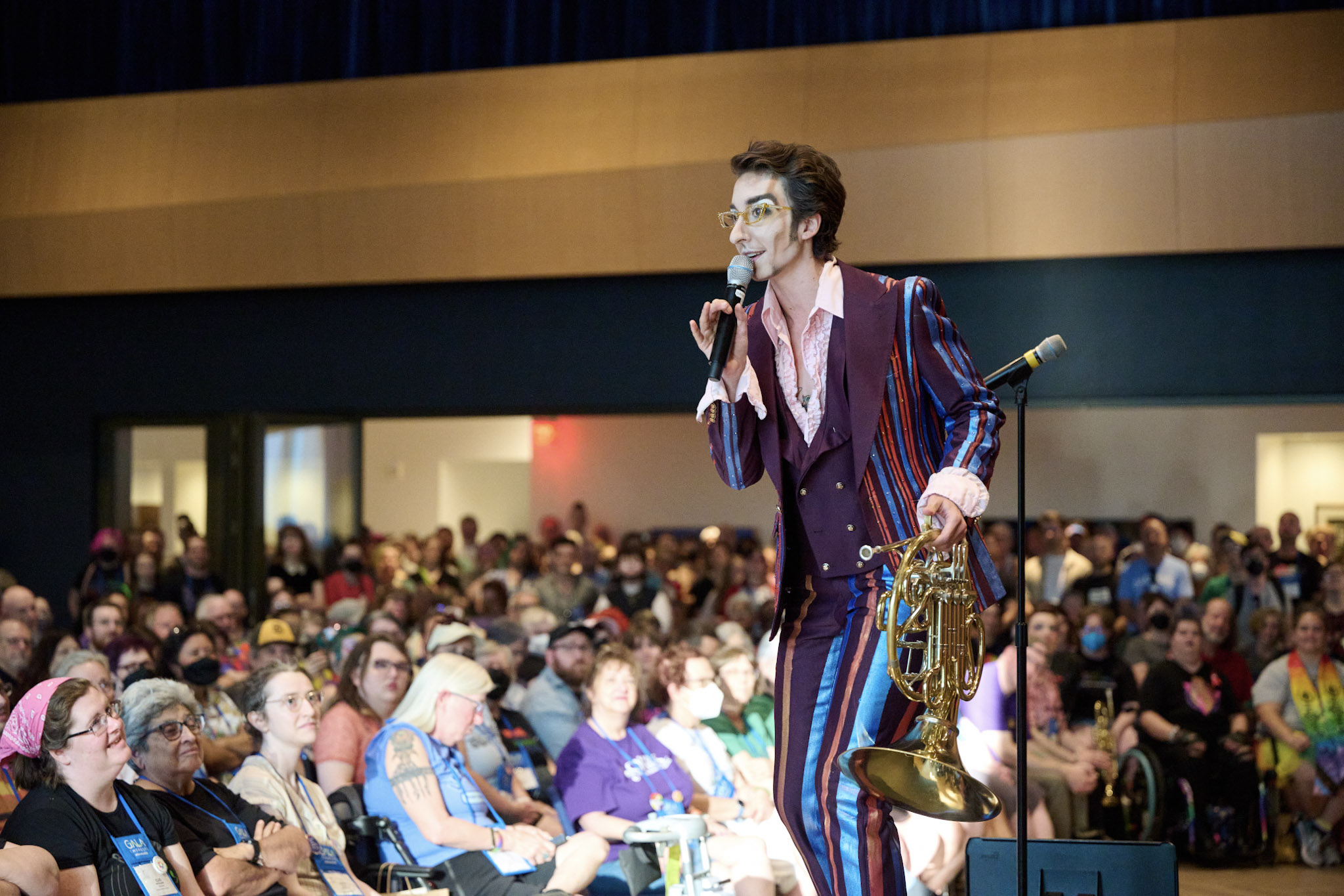 A guest artist holding a French Horn and wearing a striped suit performs at Festival 2024.