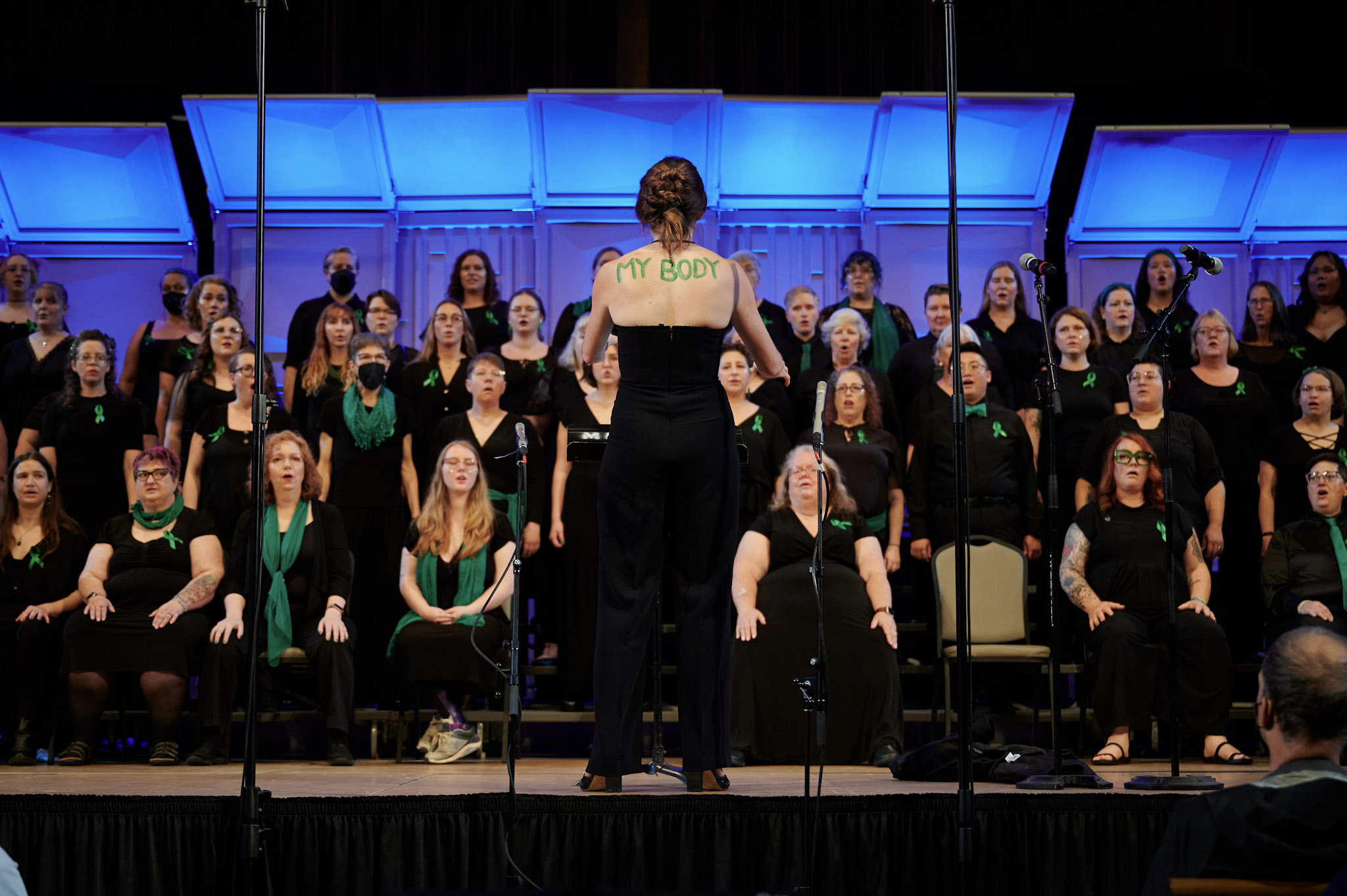 With the words, "My Body" painted in green on her back, Clelyn Chapin conducts the Denver Women's Chorus at Festival 2024.