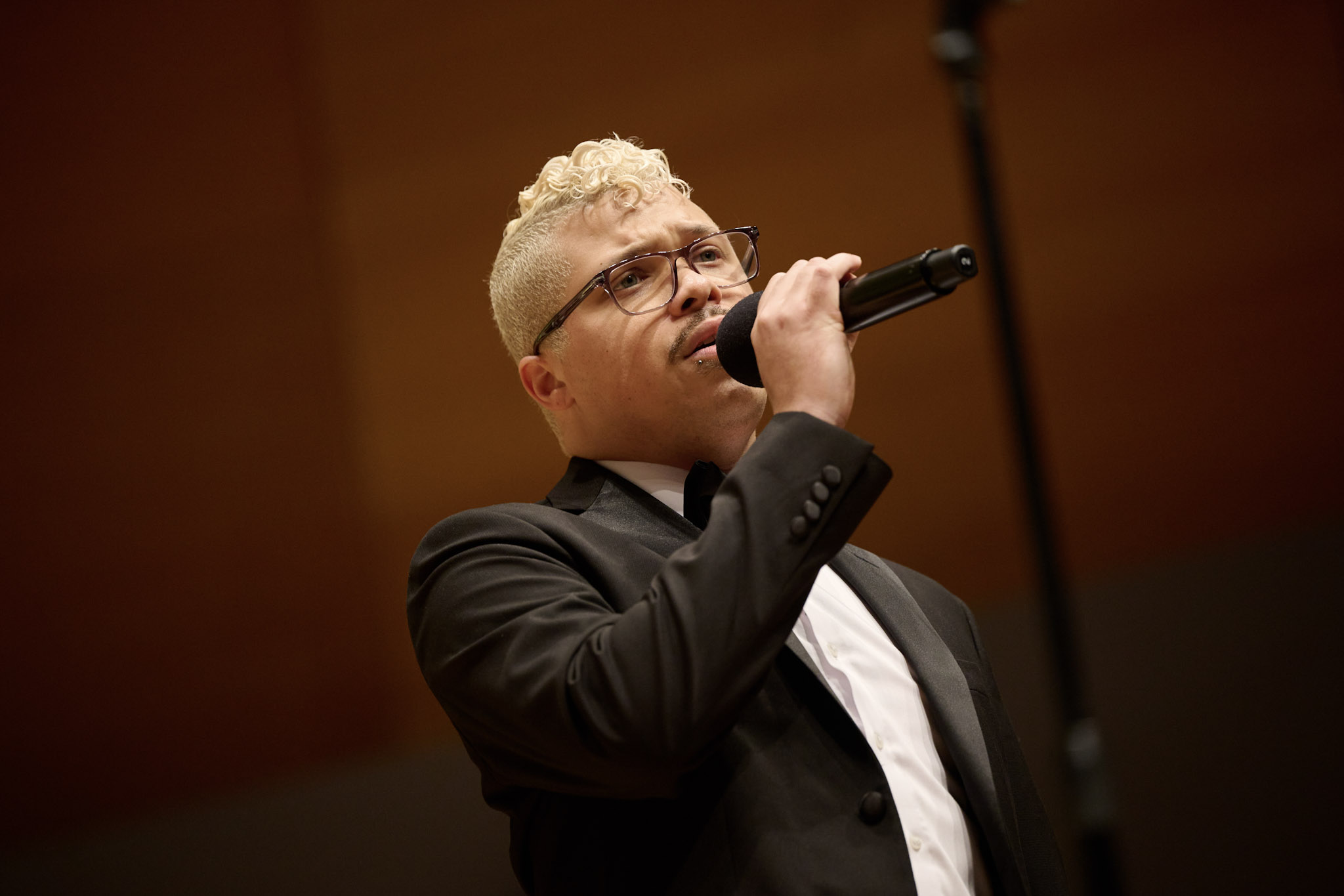 A singer with blonde hair and wearing a tux sings into a mic at Festival 2024.