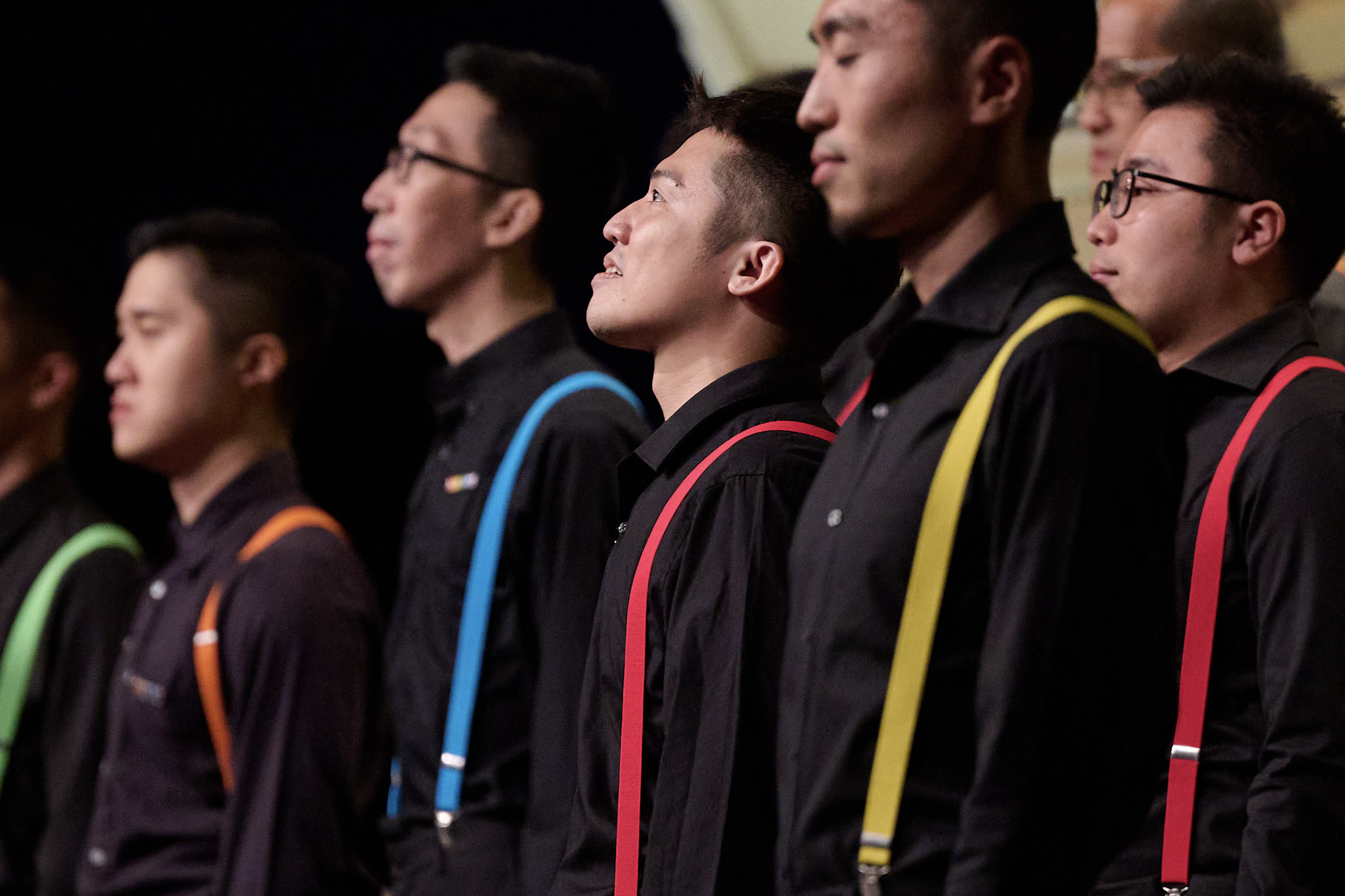 A choir at Festival 2024 performs wearing black and colorful suspenders.