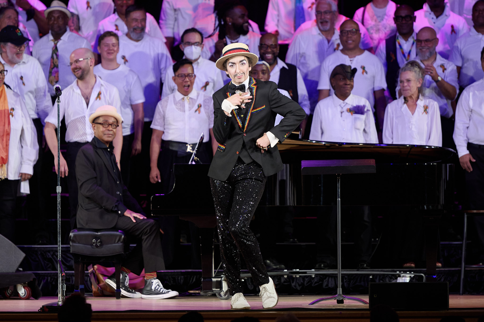 A performer wearing a boater's hat and sparkly suit performs in front of a choir wearing white shirts at Festival 2024.