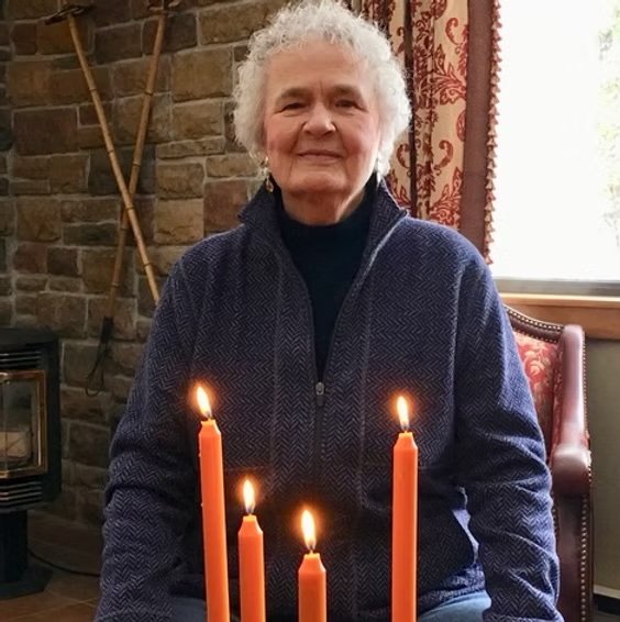 Judith Nelson, an elder woman with silver hair, stand in front of four lit candles.