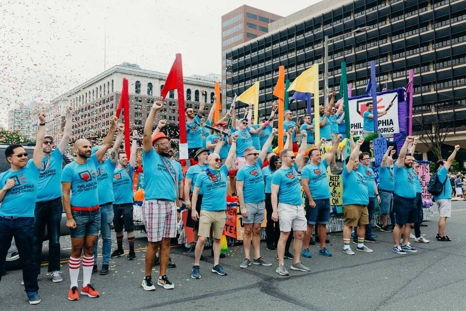 group of male presenting people with teal tshirts on the street raising flags