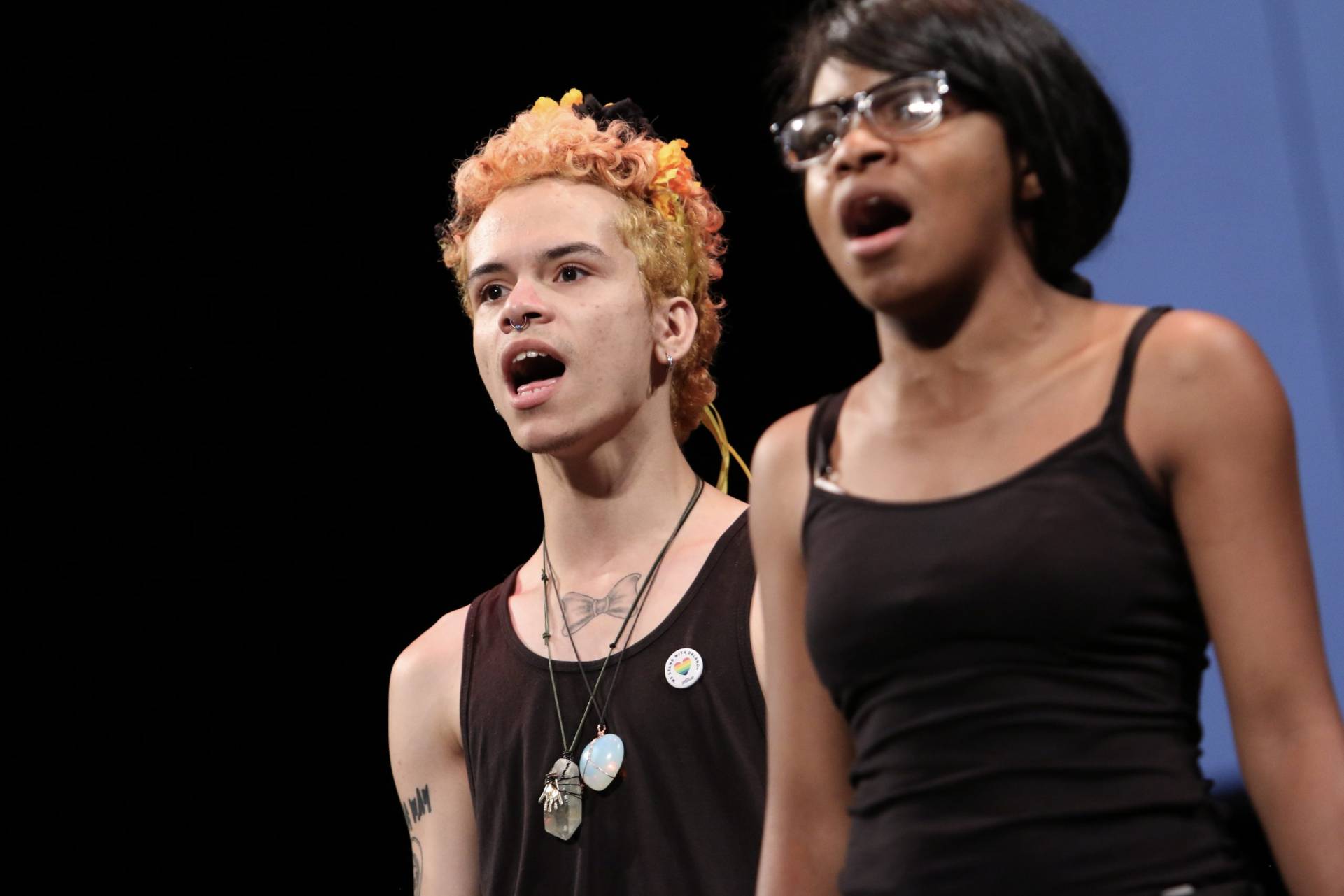Two singers - one with a nose ring, dyed hair, and tattoo and other young black female presenting person